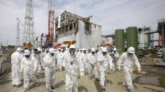 Members of the media and Tokyo Electric Power Co. (TEPCO) employees, wearing protective suits and masks, walk in front of the No. 4 reactor building at the tsunami-crippled Fukushima Daiichi nuclear p