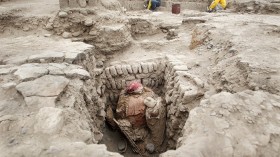 People work near an intact mummy of the Wari prehispanic culture, seen inside a recently discovered tomb, in Lima's Huaca Pucllana ceremonial complex October 20, 2010. 