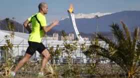 A man jogs on a sunny day as the Olympic Cauldron and flame are seen in the background in the Olympic Park during the 2014 Winter Olympic Games February 12, 2014. 