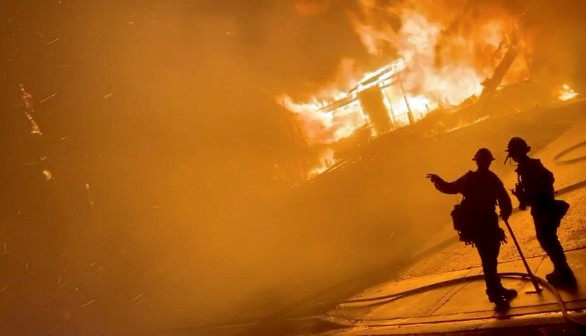 A firefighter gestures to a colleague in front of a house on fire during wildfires in California