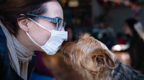 Woman with mask kissing dog.