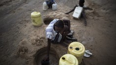 Woman scoops water from a dry river bed 