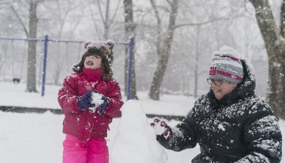 Girl catching snowflakes with her tongue while she makes a snowman with her mother 