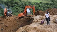 A woman stands near machinery at the scene where a mudslide buried two houses