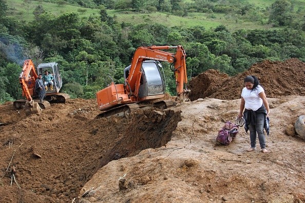 A woman stands near machinery at the scene where a mudslide buried two houses
