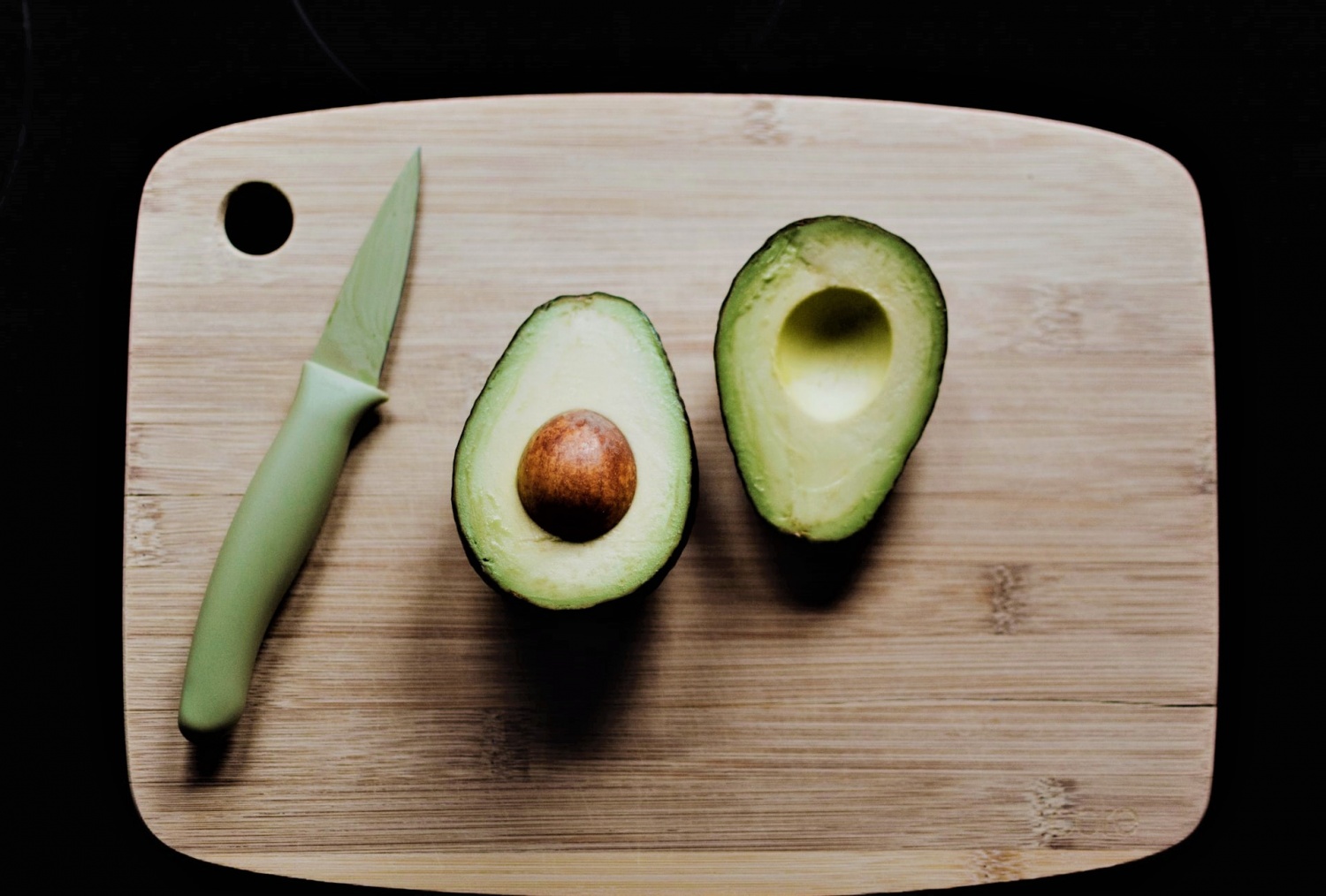 Fresh Market Avocado Cut In Half On A Wooden Cutting Board Next To A Knife  With More Avocados In The Background In A Cotton Reusable Shopping Bag  Stock Photo - Download Image