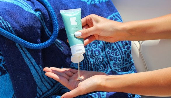 Squeezing CBD lotion into cupped hand on a boat with beach towel and rope