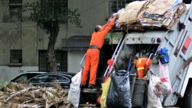 man in orange jacket and blue denim jeans standing near garbage