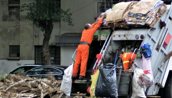 man in orange jacket and blue denim jeans standing near garbage