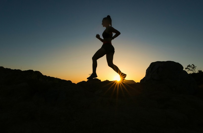A woman runs up a trail during sunset.