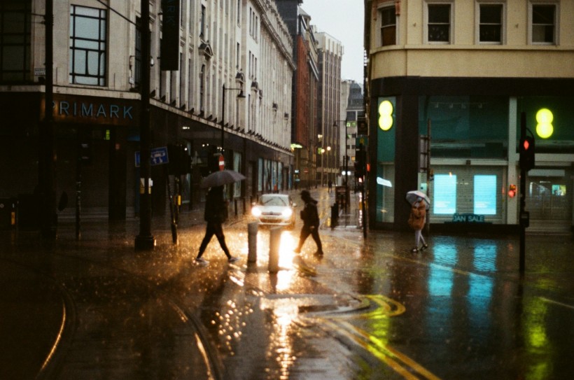  a group of people walking across a street holding umbrellas