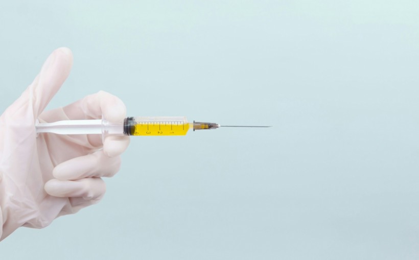 a doctor's hand in a white medical glove holding a syringe with a yellow medicine on a blue background