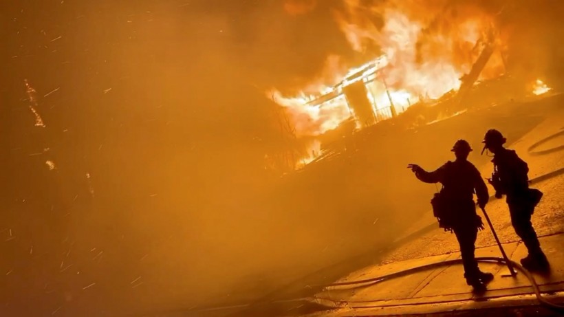 A firefighter gestures to a colleague in front of a house on fire during wildfires in California